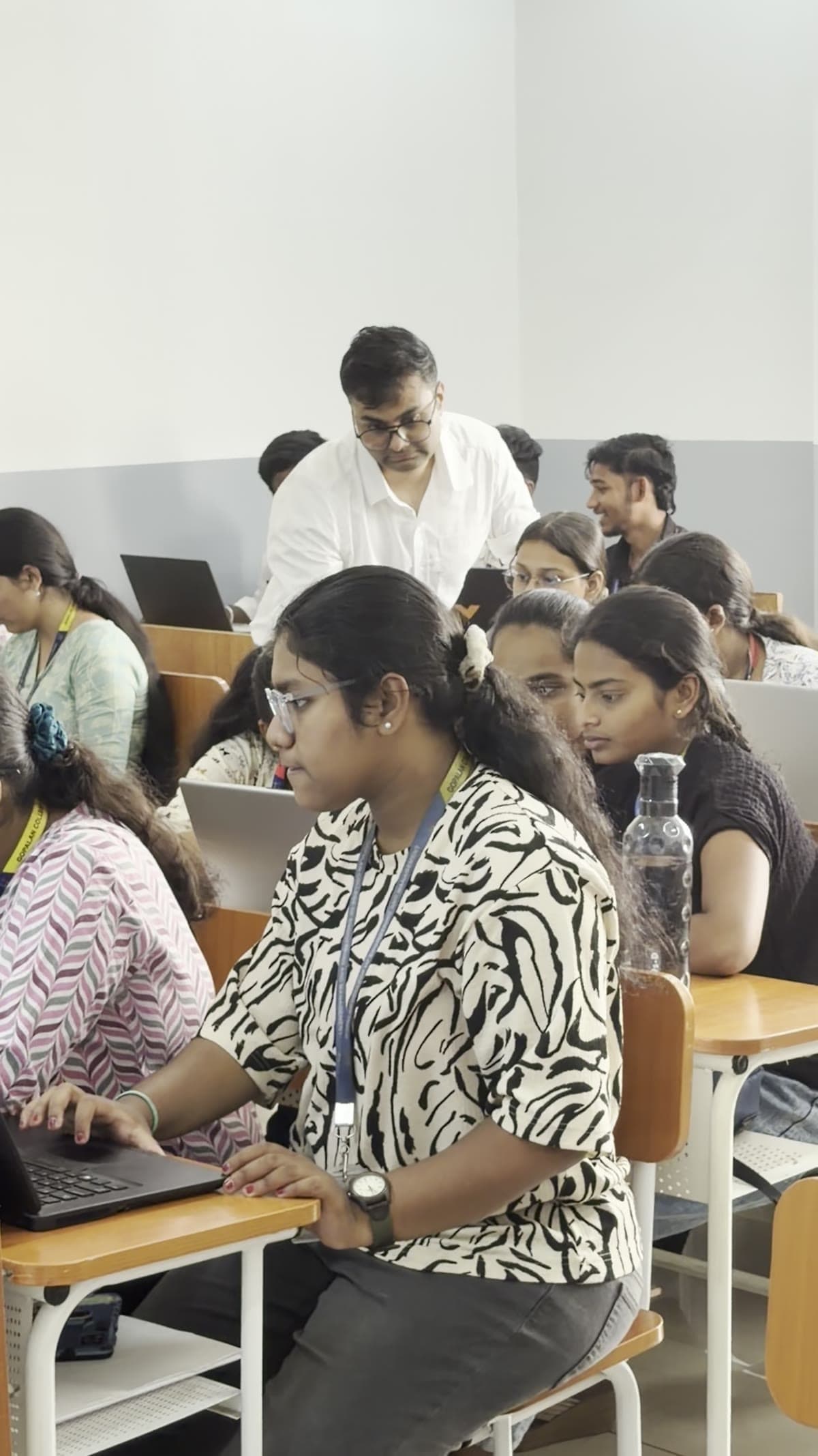 Students working on their laptops while an instructor moves through the classroom